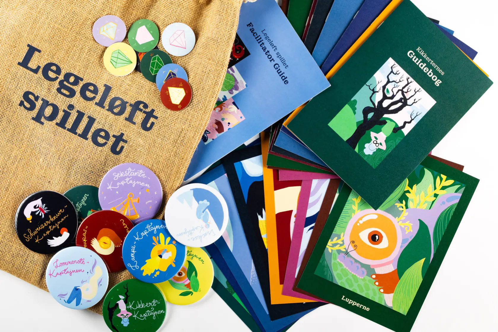 Et samlet overblik over hele legeløft spillet med jute pose, bagdes, diamantemblemer, facilitator guide, guidebog og spillekort. 
